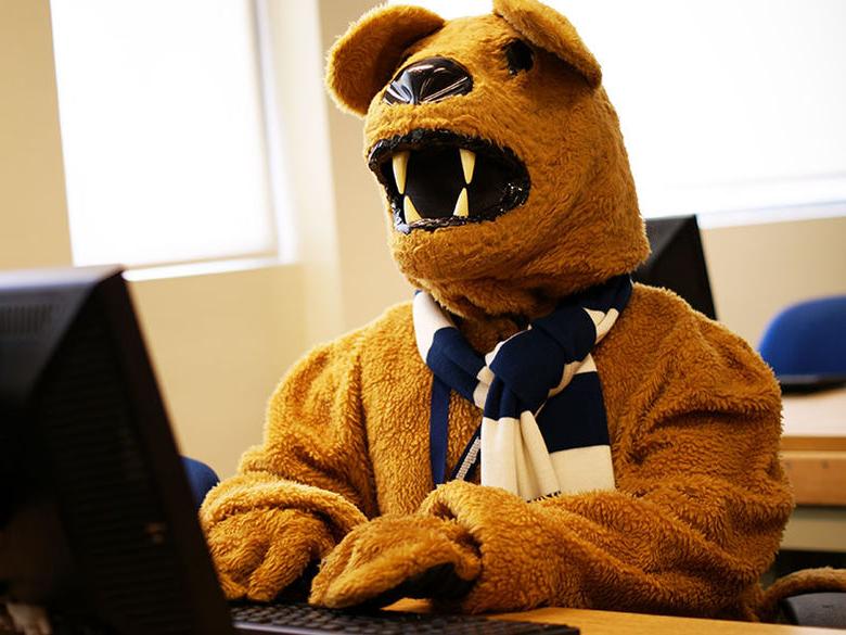 The Nittany Lion mascot looks up information on a computer in a classroom
